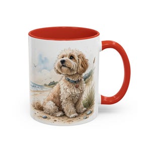 May include: White ceramic mug with a red interior and handle. The mug features a watercolor illustration of a fluffy, light brown dog sitting on a sandy beach. The dog wears a blue collar with a heart-shaped tag. The background shows a beach scene with grass and a cloudy sky.