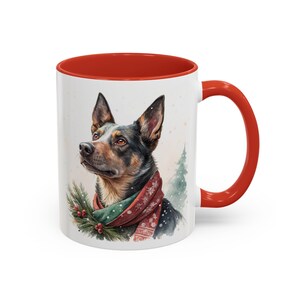 May include: White ceramic mug with a red interior and handle. The mug features a watercolor illustration of a dog wearing a festive scarf and a sprig of greenery. A Christmas tree is in the background.