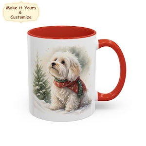 Peut inclure: Mug en céramique blanche avec intérieur et anse rouges. L'illustration représente un chien blanc et duveteux portant une écharpe rouge et verte, dans une scène enneigée avec un sapin de Noël. Le texte en haut à gauche dit "Make it Yours & Customize".