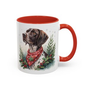 May include: White ceramic mug with a red interior and handle. The mug features a watercolour illustration of a dog wearing a red bandana with a Christmas design. Greenery and red berries surround the dog.