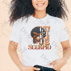 May include: White t-shirt with a graphic of a Black woman with an orange headband and glasses. The text "They Not Like Us Scorpio" is printed in orange on the shirt.