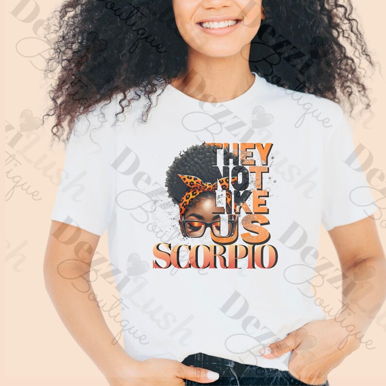 May include: White t-shirt with a graphic of a Black woman with an orange headband and glasses. The text "They Not Like Us Scorpio" is printed in orange on the shirt.