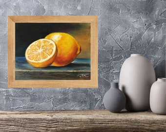 May include: A framed still life painting of two lemons. One lemon is whole, and the other is cut in half, revealing the juicy interior. The artwork is set against a dark background with a blue surface.
