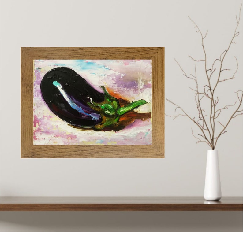 May include: Oil painting of an eggplant in a wooden frame. The eggplant is dark purple with a green stem and sits on a background of pink, white, and purple brushstrokes. The frame is a light brown color.