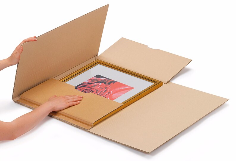 May include: A framed picture with a red rose is being carefully placed into a cardboard box with a protective layer of cardboard.