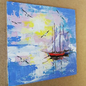 May include: A painting of a sailboat with white sails on a blue and pink sky with white clouds. The sailboat is red and black and is reflected in the water. There are seagulls flying in the sky.