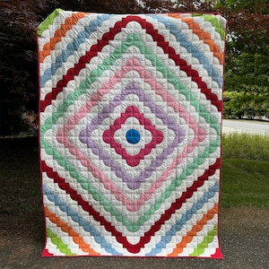 May include: A colorful quilt with a diamond pattern made of scalloped shapes in shades of red, orange, yellow, green, blue, pink, and purple. The center of the quilt features a large flower with a blue circle in the middle.