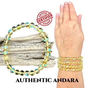Pode incluir: Pulseiras de contas amarelas e iridescentes. As pulseiras são exibidas em um pedaço de madeira e em um pulso. O texto "AUTHENTIC ANDARA" está na parte inferior da imagem, com um selo "CERTIFIED".