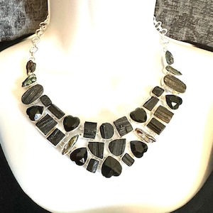 May include: A silver chain necklace with a black and green gemstone pendant. The pendant is made up of multiple stones, including black onyx and black tourmaline.
