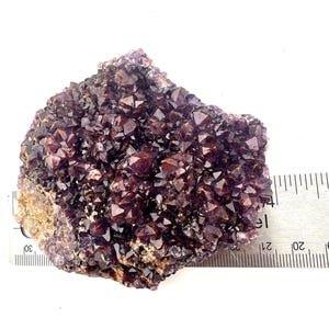 May include: A cluster of amethyst crystals with a deep purple color and a hint of red. The crystals are clustered together in a rough, natural formation. The crystals are approximately 2 inches in diameter.