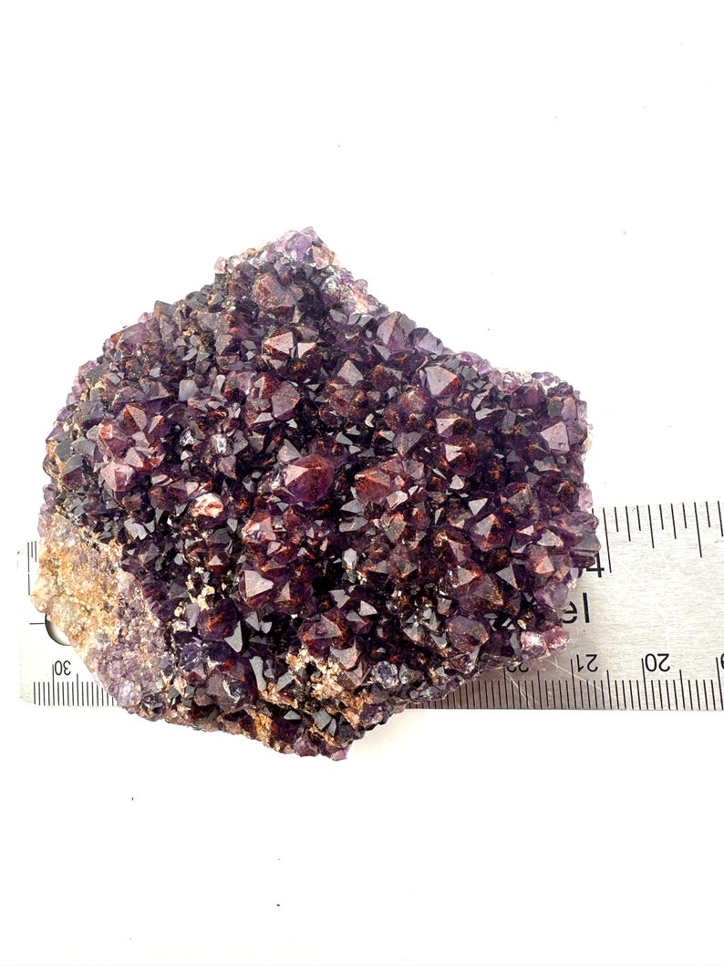 May include: A cluster of amethyst crystals with a deep purple color and a hint of red. The crystals are clustered together in a rough, natural formation. The crystals are approximately 2 inches in diameter.