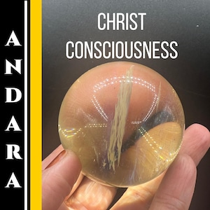 May include: A clear, round crystal sphere with internal white veining is held in a hand. The sphere reflects light, creating a shimmering effect. The text "CHRIST CONSCIOUSNESS" is above the sphere, and the word "ANDARA" is vertically aligned on the left side.