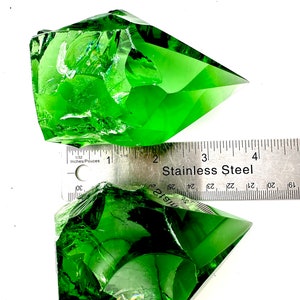 May include: Two large, green, faceted crystal points, one partially resting on a stainless steel ruler marked in inches. The ruler reads "Stainless Steel" and has markings from 1 to 4 inches.