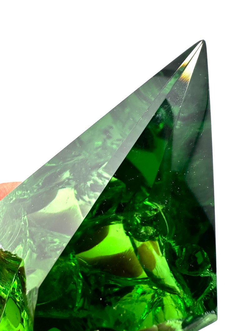 May include: A large, faceted, green crystal pyramid with a sharp point.