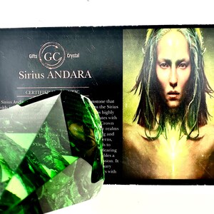 May include: A green, faceted, crystal gemstone with the text "Sirius Andara" and "Certified Authentic" on a black card with a woman's image.
