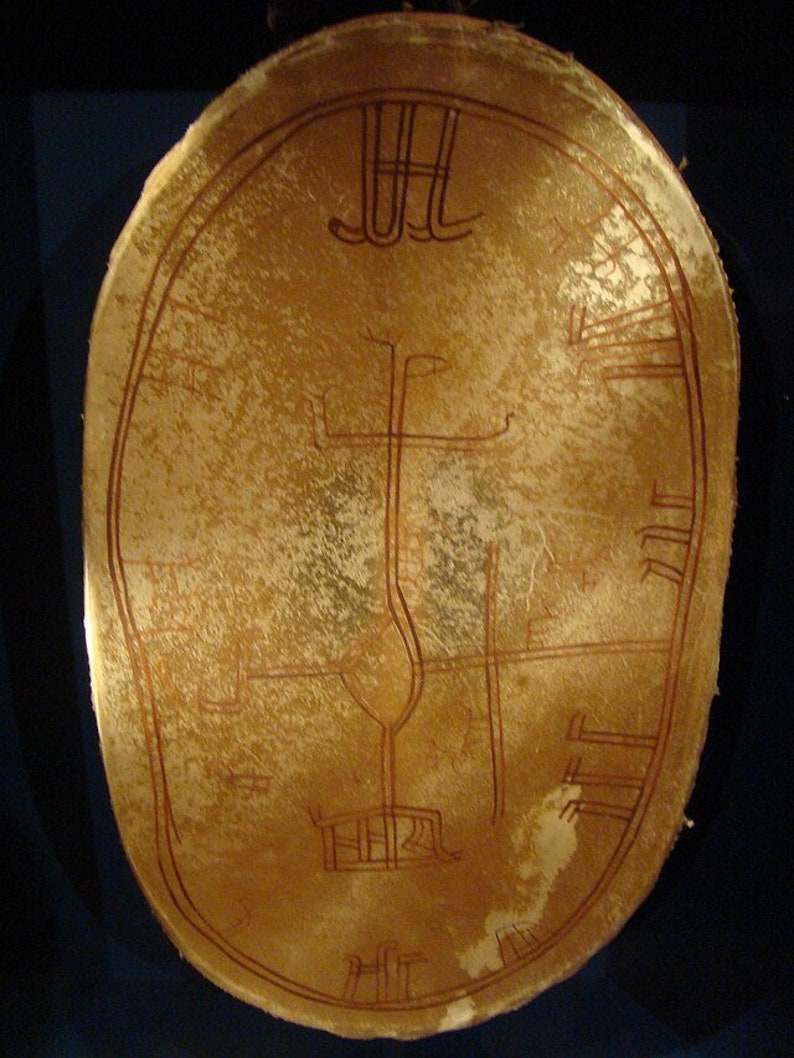 May include: A tan, oval-shaped artifact with intricate, reddish-brown line drawings. The design includes a central vertical line, a curved shape, and several horizontal and vertical lines, possibly depicting a map or symbolic representation. The object has a textured surface.
