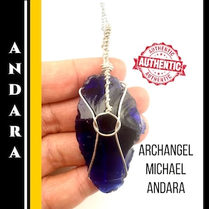 Puede incluir: Colgante de cristal Andara azul oscuro con un alambre de plata. El colgante tiene la forma de una piedra en bruto. El texto "ARCHANGEL MICHAEL ANDARA" es visible. También es visible un sello rojo "AUTHENTIC".