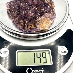 May include: A large amethyst crystal cluster weighing 149 grams. The cluster is a deep purple color and has a rough, natural texture.