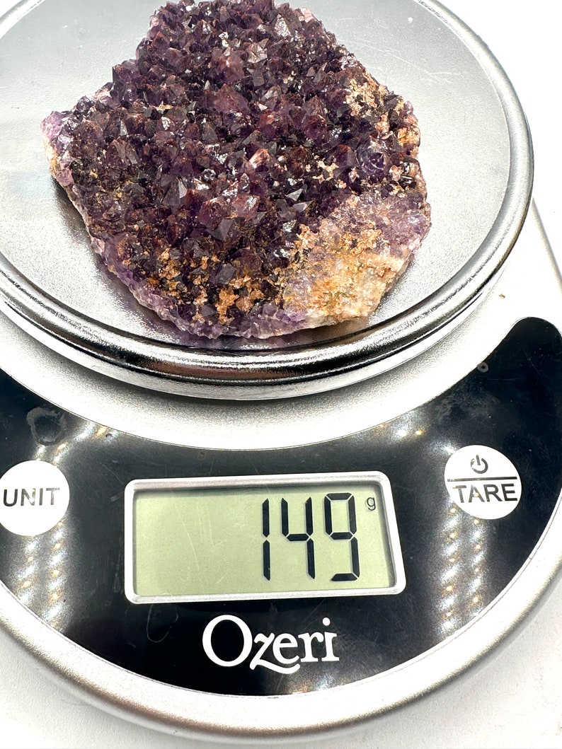 May include: A large amethyst crystal cluster weighing 149 grams. The cluster is a deep purple color and has a rough, natural texture.