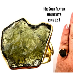 May include: A gold-plated ring featuring a large, green, irregularly shaped moldavite stone. The ring is size 7. 18k Gold Plated Moldavite Ring Sz 7.