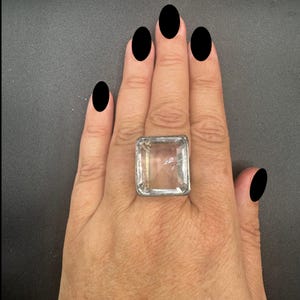 Puede incluir: Un anillo de plata con una gran piedra preciosa cuadrada transparente.