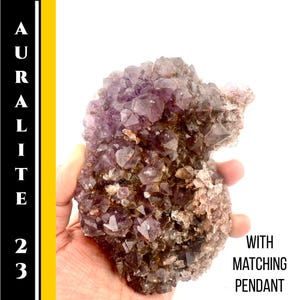 May include: Auralite 23 crystal cluster with a mix of purple and brown hues. The image includes the text "AURALITE 23" vertically on the left side and "WITH MATCHING PENDANT" on the right.