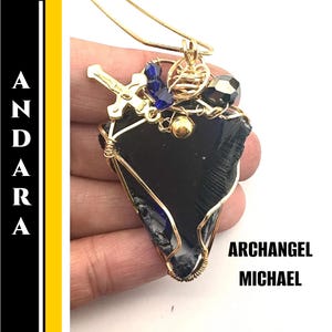 May include: A handcrafted pendant featuring a dark blue, irregularly shaped stone wrapped in gold-colored wire. The pendant is adorned with a gold cross, blue beads, and a gold-colored chain. The text "ARCHANGEL MICHAEL" is visible.