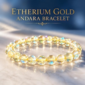 May include: A bracelet made of translucent, pale yellow spherical beads with an iridescent finish. The text ETHERIUM GOLD ANDARA BRACELET is displayed in gold lettering above the jewellery, which rests on a smooth, light-coloured surface.