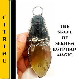 Puede incluir: Un colgante de citrino con un diseño detallado de faraón egipcio negro y plateado. El colgante tiene una piedra de citrino pulida en forma de lágrima. El texto en la imagen dice "THE SKULL OF SEKHEM EGYPTIAN MAGIC".