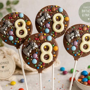 May include: Four chocolate lollipops with a brown base, decorated with colourful sprinkles, candies, and a white number 8. Each lollipop has a silver-coloured car and is on a white stick. The image includes the text "PERFECT FOR BIRTHDAYS & PARTIES!"