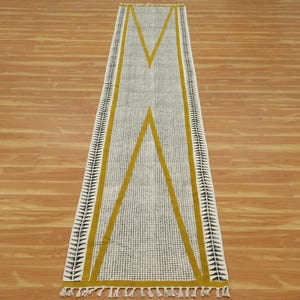 Könnte beinhalten: Ein weißer und schwarzer gemusterter Läufer mit gelben Streifen. Der Läufer hat ein geometrisches Muster mit einer zentralen X-Form.