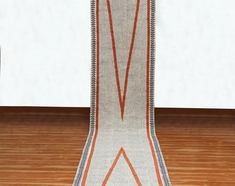 Puede incluir: Una alfombra de pasillo blanca con un patrón geométrico en naranja y negro. La alfombra tiene un borde de flecos.