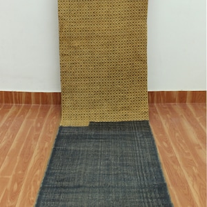 May include: A long, rectangular rug with a two-toned design. The top half is a light yellow with a dark brown chevron pattern. The bottom half is a dark blue with a subtle texture. The rug has a fringe border.