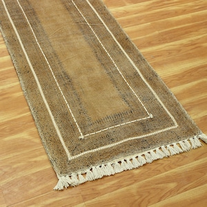 Könnte beinhalten: Ein brauner Läuferteppich mit einem geometrischen Muster in Schwarz und Weiß und Fransen an den Enden.