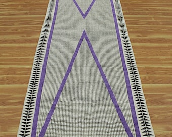 Puede incluir: Una alfombra de pasillo larga y rectangular con fondo blanco y un patrón geométrico. El patrón presenta una gran X púrpura en el centro, con triángulos negros y blancos en los bordes.
