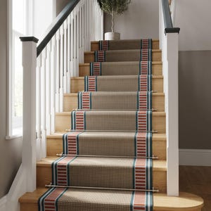 May include: A staircase runner featuring a tan base with a small white dot pattern, bordered by vertical stripes in red, white, and dark blue. The runner is secured to the wooden stairs with horizontal silver metal rods at each step riser.