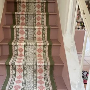 May include: A set of stairs with a pink painted surface and a green and pink patterned runner. The runner has a geometric design with a repeating pattern of diamonds and lines.