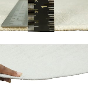 Op de afbeelding: Close-up van een wit tapijt met een liniaal die 7,6 cm meet. Het tapijt heeft een zachte, pluche textuur.