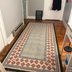 May include: A green, red, and white patterned rug with a geometric design. The rug is laid out on a wooden floor in a hallway.