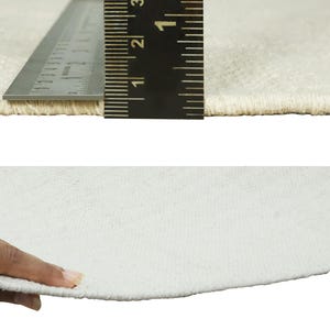 May include: Close-up of a white rug with a ruler measuring 3 inches. The rug has a soft, fuzzy texture.