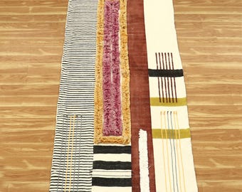 Puede incluir: Una alfombra geométrica con patrones blancos, negros y marrones con flecos en los extremos. La alfombra tiene una variedad de texturas, incluyendo rayas, cuadrados y círculos.