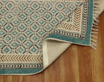 May include: A blue and brown patterned rug with fringe on the edges. The rug is folded in half and the underside is visible.