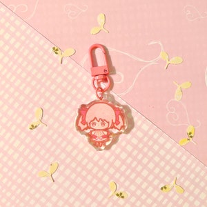 K&ouml;nnte beinhalten: Rosaer Anime-Charakter-Schl&uuml;sselanh&auml;nger mit Glitzerakzenten. Der Schl&uuml;sselanh&auml;nger zeigt ein kleines, cartoonartiges M&auml;dchen mit Z&ouml;pfen und einem rosa Kleid. Der Schl&uuml;sselanh&auml;nger ist an einem rosa Metallverschluss befestigt.