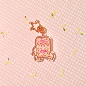 Pu&ograve; includere: Un portachiavi a forma di cartone di latte Hello Bunbun rosa e bianco con un ciondolo a stella dorata. Il portachiavi presenta un coniglio dei cartoni animati con naso e orecchie rosa, e il testo "Hello Bunbun" in lettere rosa.