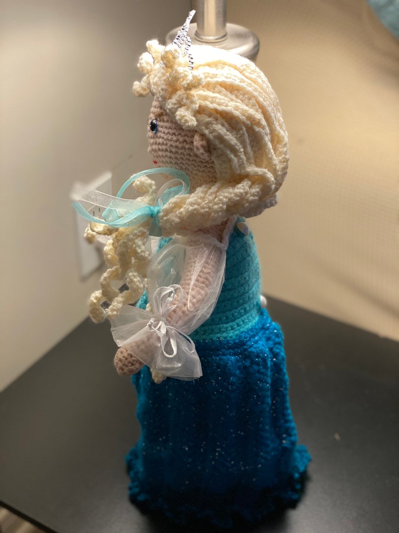 May include: A crocheted doll with long blonde hair, wearing a blue and white dress with a white crown on her head.