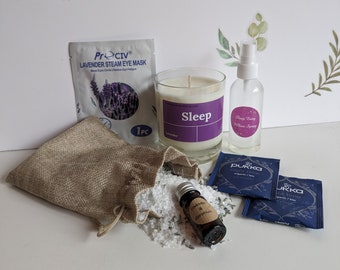 May include: A collection of self-care items for relaxation and sleep. The items include a lavender steam eye mask, a candle with the word "Sleep" on it, a bottle of sleep pillow spray, a burlap bag filled with bath salts, a small bottle of lavender and geranium essential oil, and two blue tea bags.