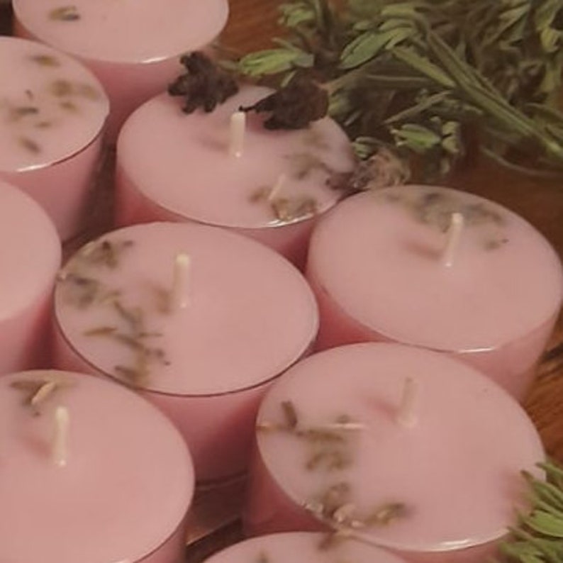 May include: A group of pink tea light candles with dried lavender flowers embedded in the wax. The candles are arranged in a circle.