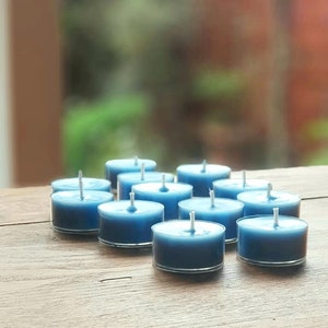 May include: A group of blue teal tea light candles arranged on a wooden surface.