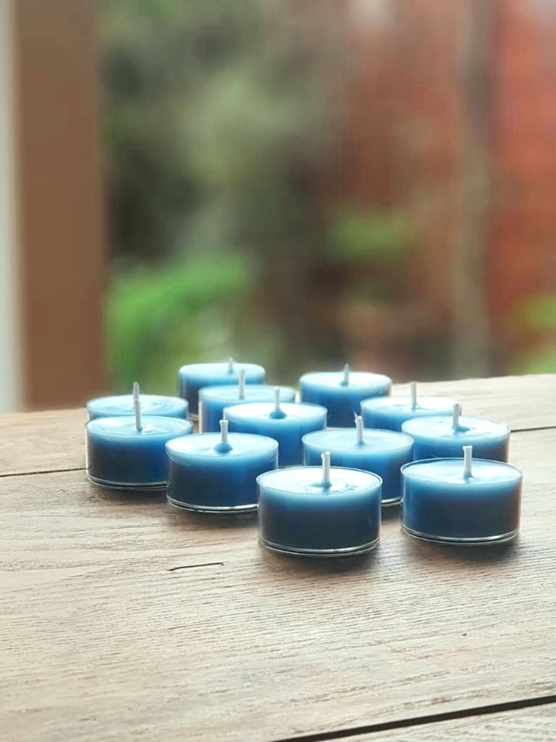 May include: A group of blue teal tea light candles arranged on a wooden surface.