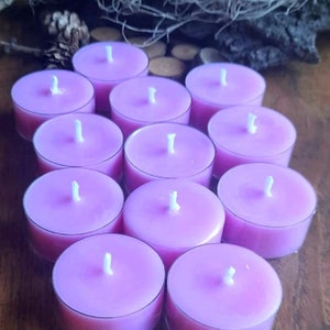 May include: A group of 10 lavender-colored tea light candles arranged in a circle on a wooden surface. The candles are unscented and have a white wick in the center.